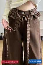 Person wearing a plaid shirt over brown pants with a visible brand logo at the bottom.