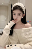 Woman wearing a white off-shoulder sweater with black buttons indoors.