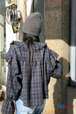 Person wearing a plaid shirt and gray beanie standing against a wall with 'TOMS CLOTH' branding.