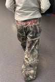 Person wearing camouflage pants with a visible brand logo on a gray floor.