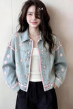 Woman wearing a light blue denim jacket with floral embroidery against a plain background