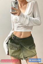Person wearing a white long-sleeve top and green denim skirt, taking a mirror selfie.