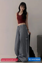 Woman wearing a red top and gray wide-leg pants against a plain background