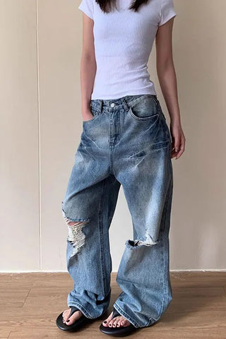 Person wearing a white t-shirt and blue jeans with rips against a plain background