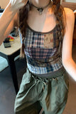 Person wearing a patchwork tank top and green pants indoors.