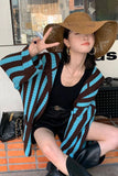 Person wearing a striped cardigan and wide-brimmed hat in an urban setting