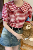 Person wearing a red and white checkered shirt with puffed sleeves, holding a teddy bear.