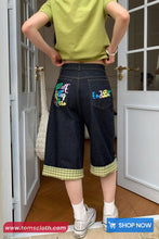 Person wearing dark blue shorts with colorful text and patterns, standing in a doorway.