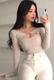 Woman taking a selfie with a phone, wearing a beige long-sleeve top and white pants.