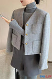 Person wearing a gray blazer with gold buttons and holding a phone.