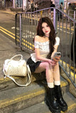 Woman sitting on steps using a phone with a white handbag beside her