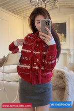 Woman taking a mirror selfie wearing a red sweater with white patterns in a room.