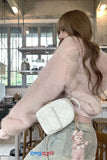 Person wearing a pink fluffy jacket with a white quilted handbag in an indoor setting.