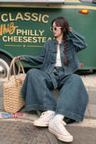Woman in denim outfit sitting on a curb with a green food truck in the background