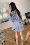 Woman taking a mirror selfie wearing a blue striped shirt dress in a room with wooden flooring.