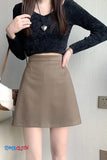Person wearing a black cropped sweater and brown skirt with a neutral background