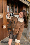 Woman in a brown jacket with white fur trim taking a selfie in front of a wooden door.