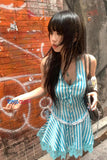Woman in a blue and white striped dress standing against a graffiti-covered wall.