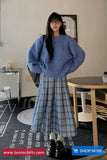 Person wearing a blue sweater and plaid skirt in an indoor setting with furniture.