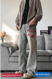 Person wearing light gray pants with red floral embroidery in a living room setting.