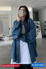 Person wearing a blue denim jacket in an indoor setting, taking a mirror selfie.