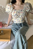 Person wearing a floral blouse and jeans sitting on a bed.