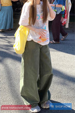 Person wearing a colorful graphic t-shirt and green pants on a street.