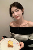 Woman holding a plate with a piece of bread, wearing an off-shoulder sweater.