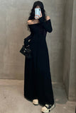 Person wearing a long black dress with cut-out details, standing against a plain background.