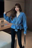 Woman in a blue denim shirt and black pants posing indoors.