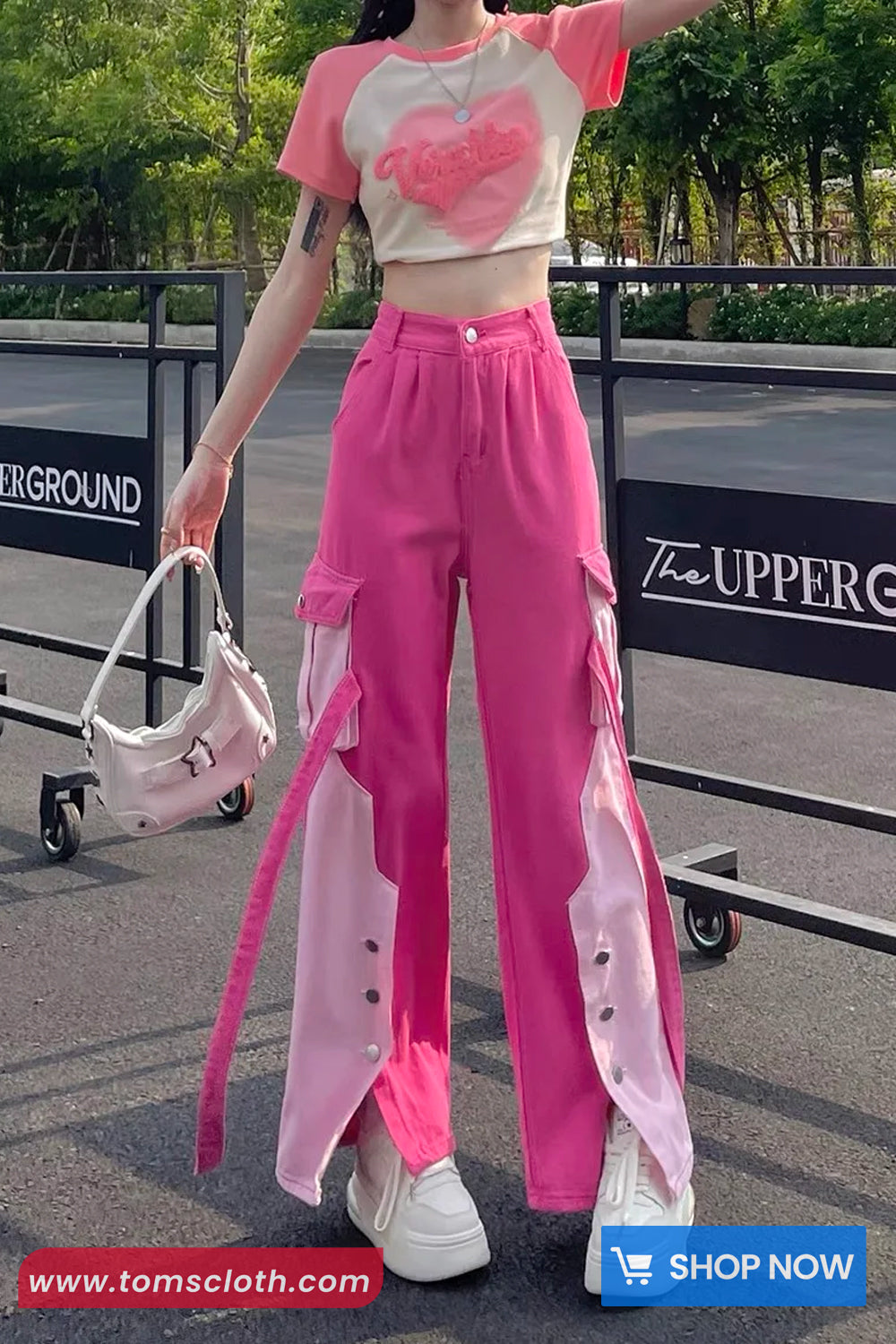 Person wearing a pink outfit with a white shirt, standing outdoors with a blurred background.