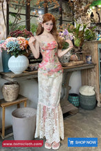 Woman in a floral dress standing in a decorative indoor setting with plants and flowers.