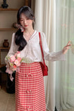 Woman in a white blouse and red checkered skirt holding flowers indoors.