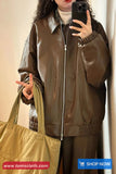 Person wearing a brown jacket holding a phone and a green bag, with 'www.tomscloth.com' branding.