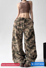 Person wearing a brown tank top and camouflage pants on a white background with 'tomscloth.com' branding.