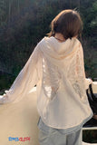 Person wearing a white lace garment with a blurred natural background