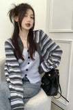 Woman wearing a striped cardigan and holding a black handbag indoors.