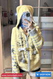 Person wearing a yellow hooded coat with decorative elements, taking a mirror selfie.