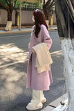 Person wearing a pink coat holding a beige bag on a street.