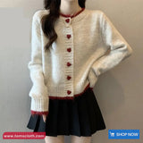 Person wearing a cream cardigan with red heart buttons on a plain background