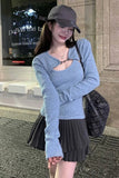 Woman wearing a light blue sweater and dark pleated skirt standing in front of a building entrance.