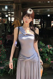 Woman in a light gray dress standing outdoors with plants and people in the background