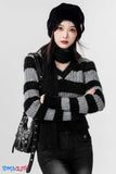 Person wearing a black and gray striped sweater with a black beanie and bag on a white background