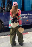 Person wearing a colorful outfit with a pink cap and green pants, standing on a street.
