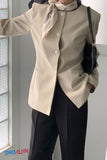 Person wearing a beige blazer and black pants with a scarf, standing indoors.
