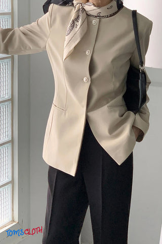 Person wearing a beige blazer and black pants with a scarf, standing indoors.