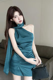 Woman in a teal dress holding a black handbag indoors.