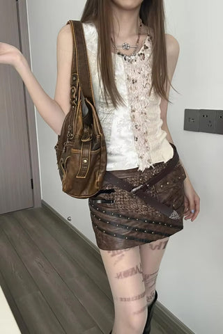 Woman holding a brown handbag indoors, wearing a white top and brown skirt.