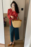 Person taking a mirror selfie wearing a red floral blouse and blue pants, holding a beige tote bag.