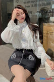 Woman wearing a white lace blouse and black skirt sitting outdoors.